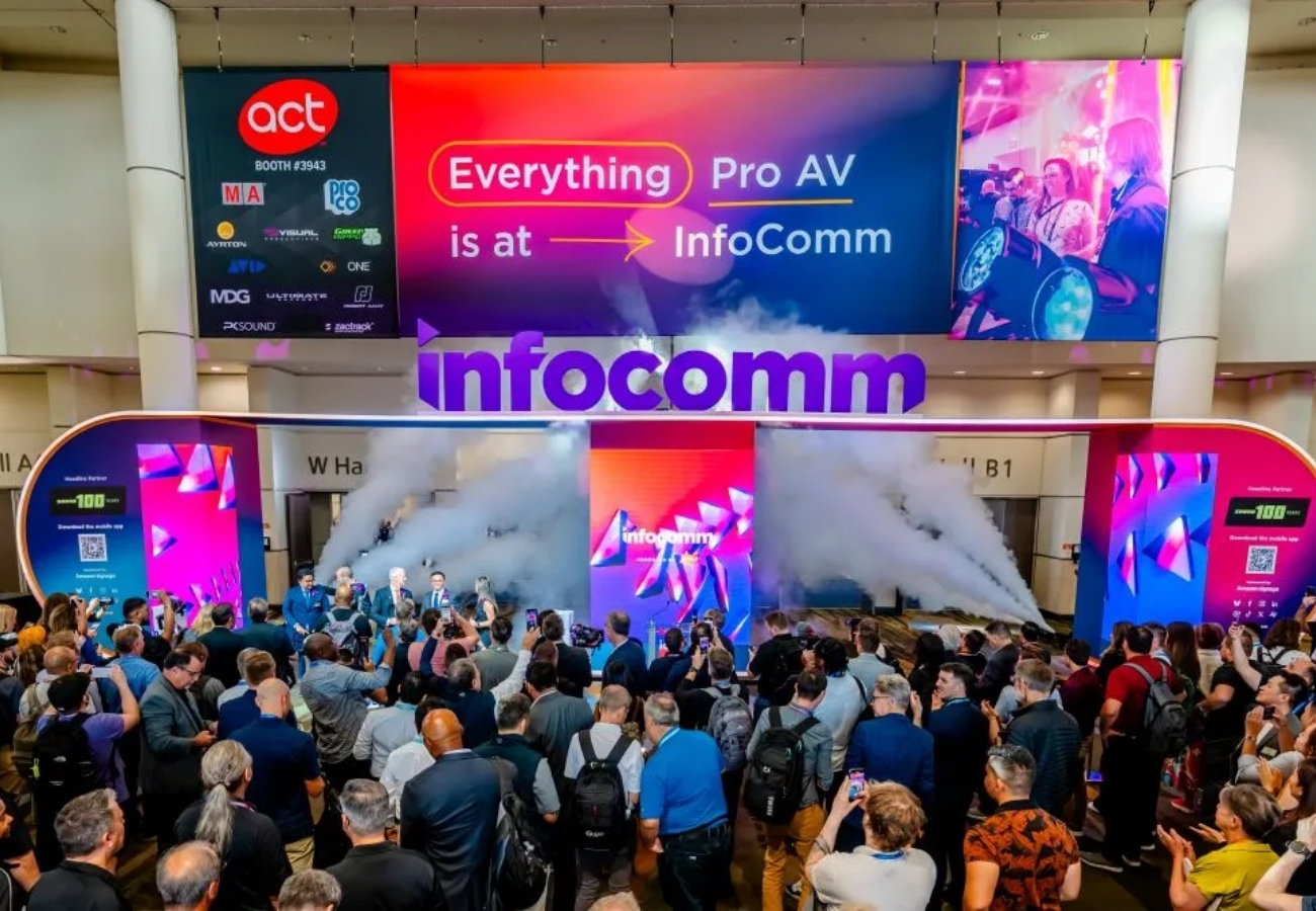 Infocomm trade show entrance with large digital signage, crowd gathering, stage presentation, and event branding at convention center