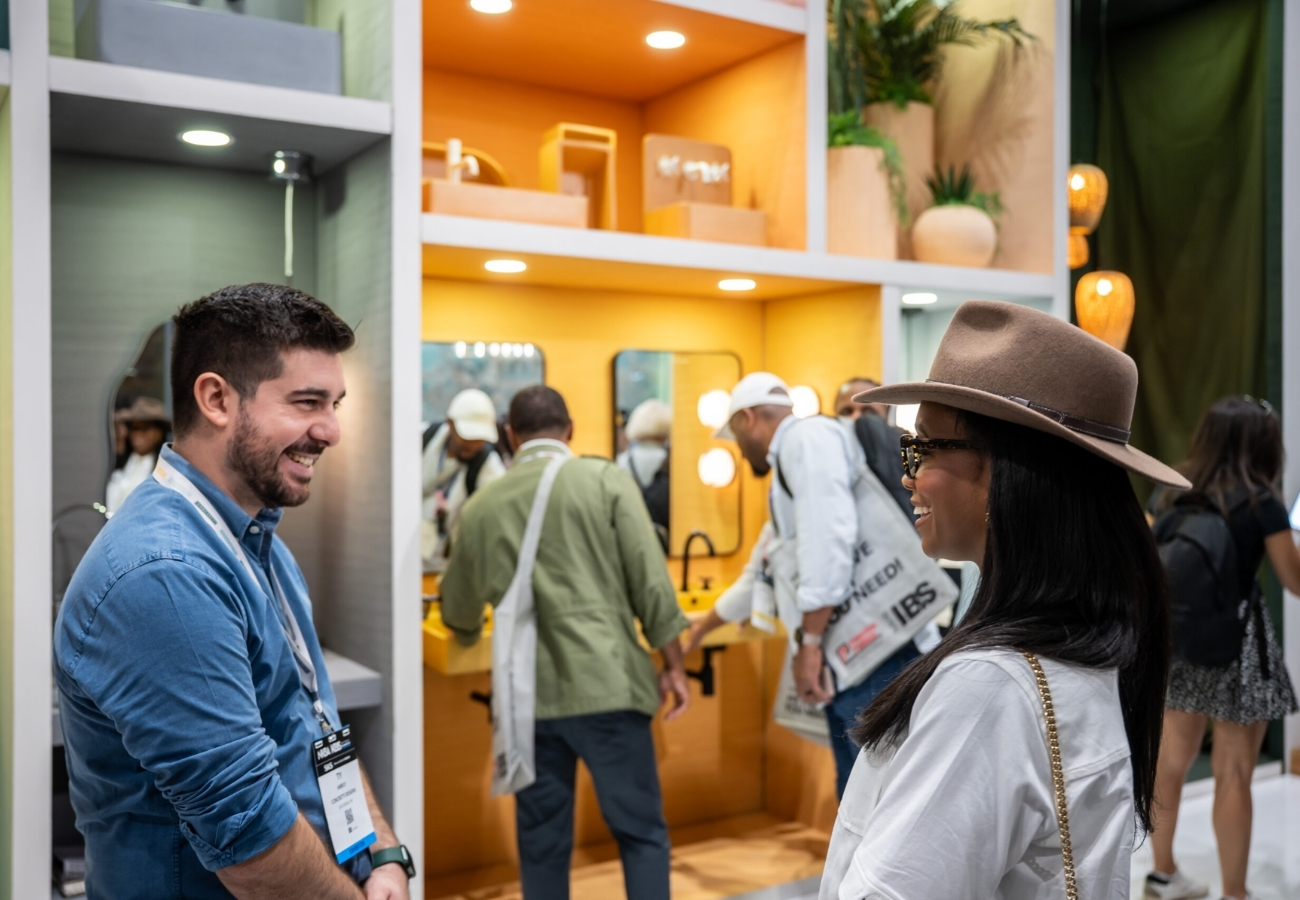 Trade show booth interaction with attendees discussing products inside modern exhibit display with lighting, mirrors, and shelving